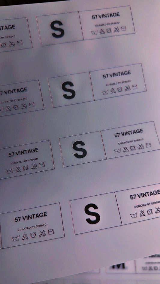 Set of 150 custom DTF clothing tags in various sizes from XS to 6X, featuring printed brand labels for apparel branding.